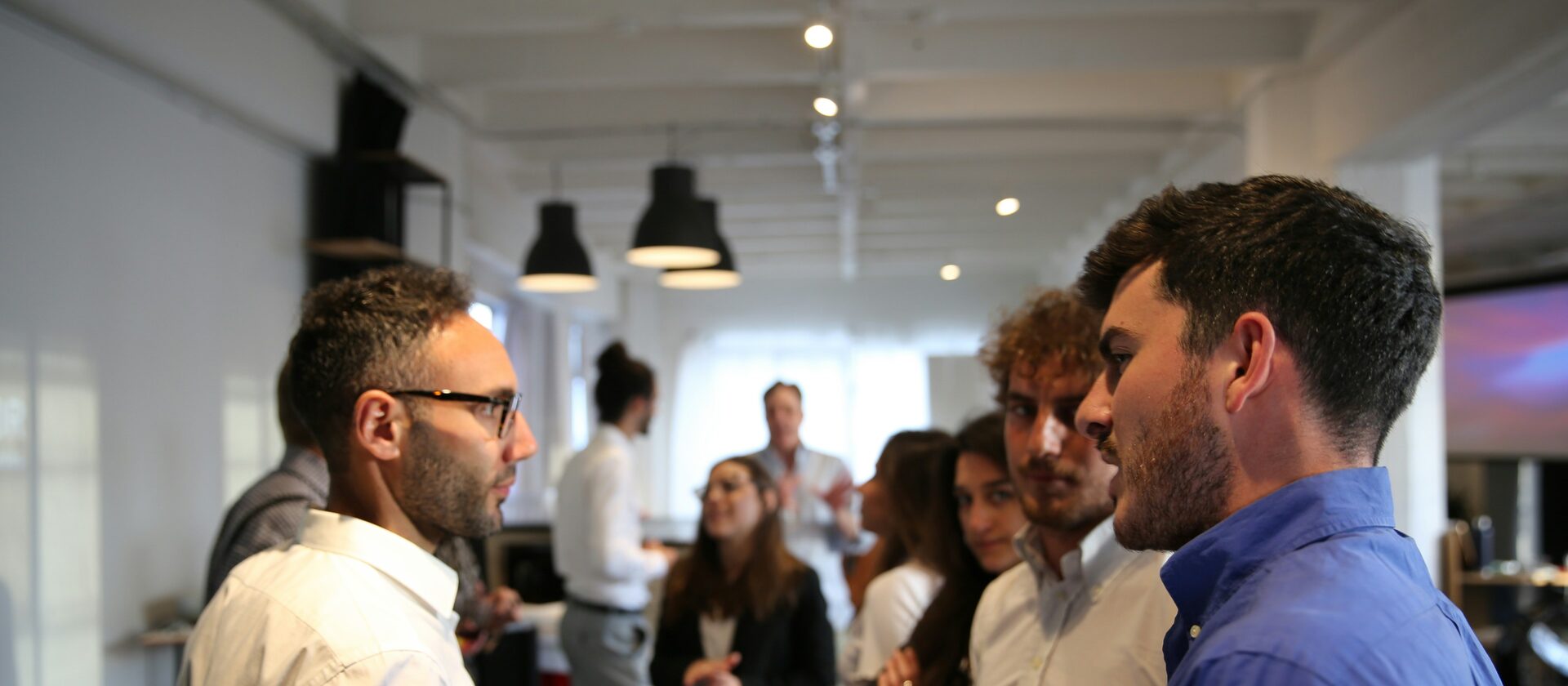 Two professionals in conversation at a networking event, with others talking behind them
